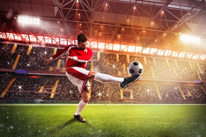 Man in red uniform kicking soccer ball in stadium