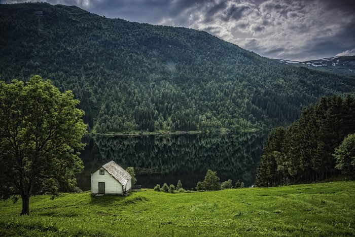 White house by a lake with forested mountains in Norway