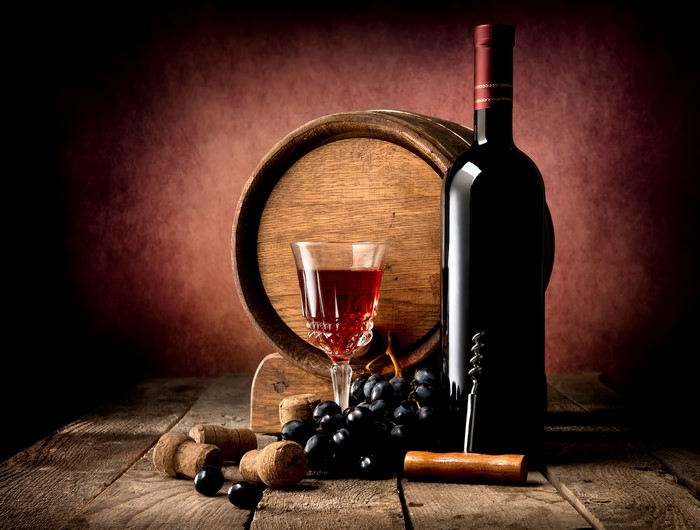 Wine bottle, glass, barrel, and grapes on wood