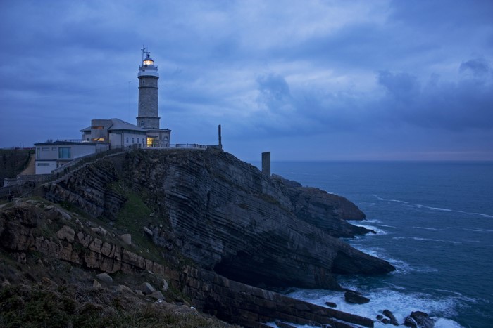 Lighthouse on a rocky cliff overlooking the sea at dusk