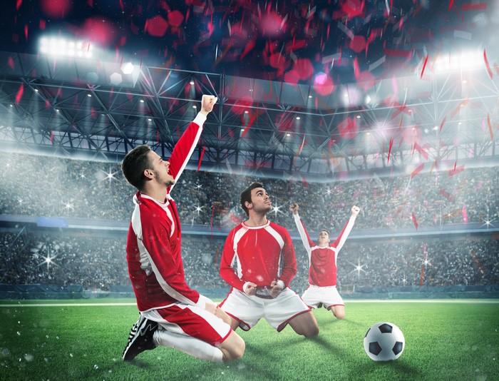Three men in soccer uniforms celebrating on a field