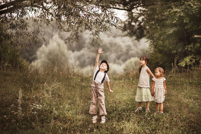 Three children reaching for tree branches in a field