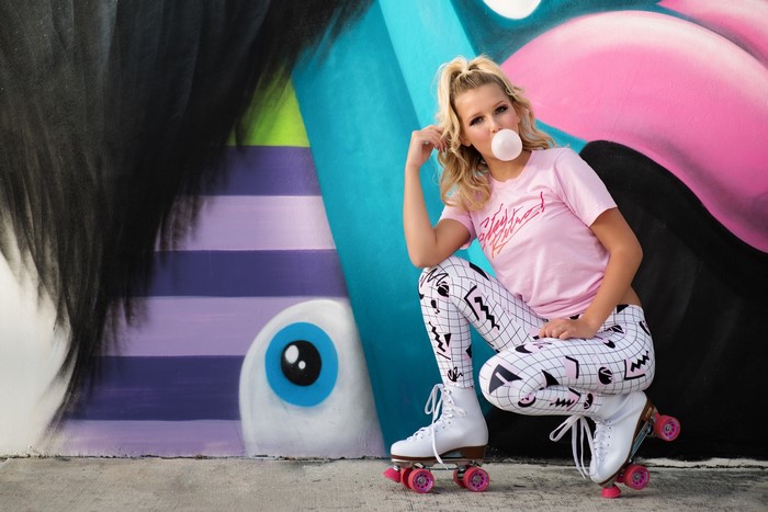 Woman in roller skates blowing bubble gum in front of graffiti art