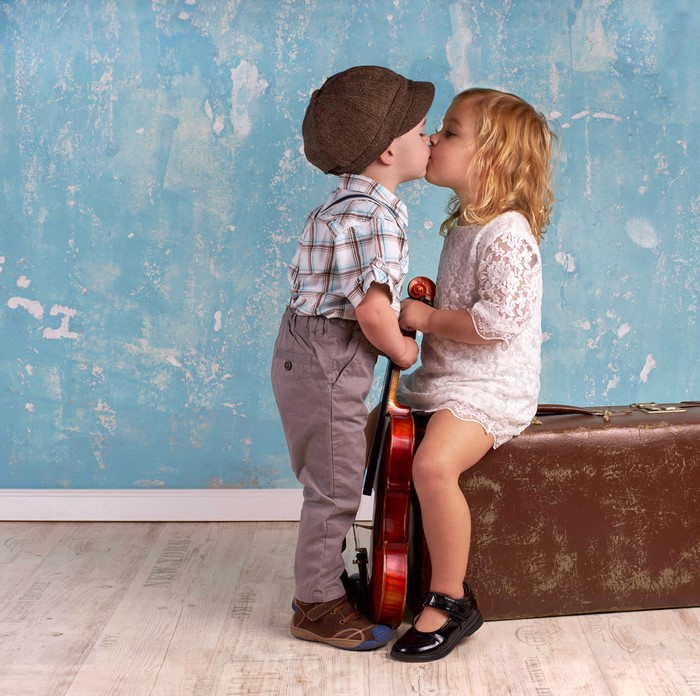 Two children kissing with a violin and suitcase