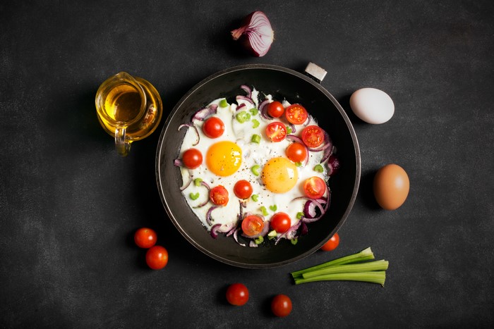 Fried eggs with tomatoes and onions in a frying pan