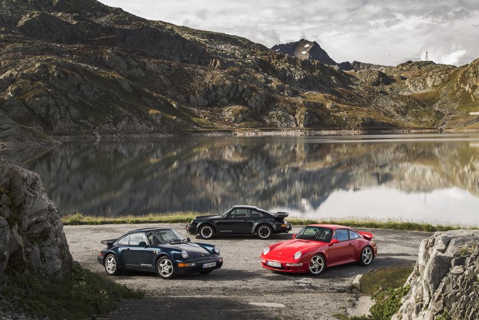 Three Porsche 911s by a mountain lake
