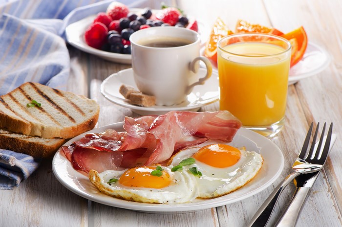 Breakfast with fried eggs, ham, bacon, toast, berries, coffee, and orange juice