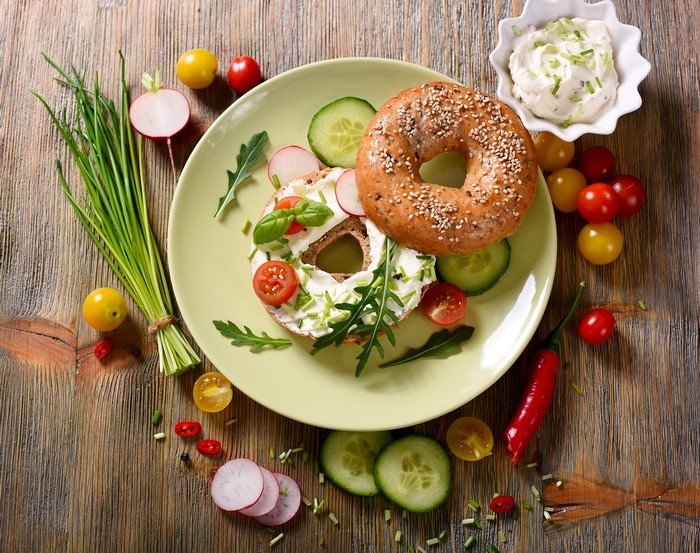Bagel with cream cheese, vegetables, and chives on a plate