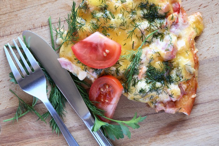 Pizza with tomatoes and dill, fork and knife