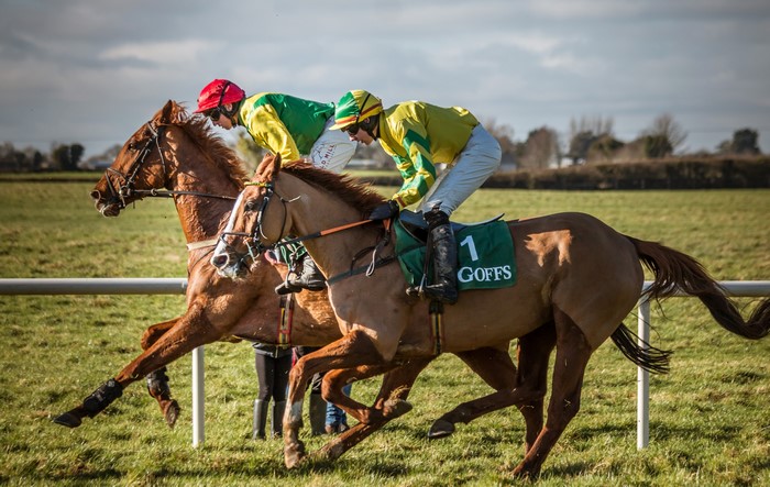 Two jockeys racing horses with green saddle cloths