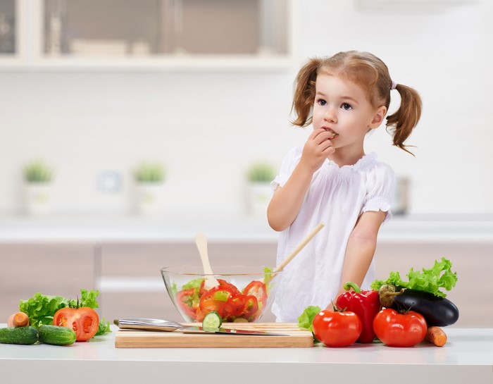 Little girl eating salad in kitchen