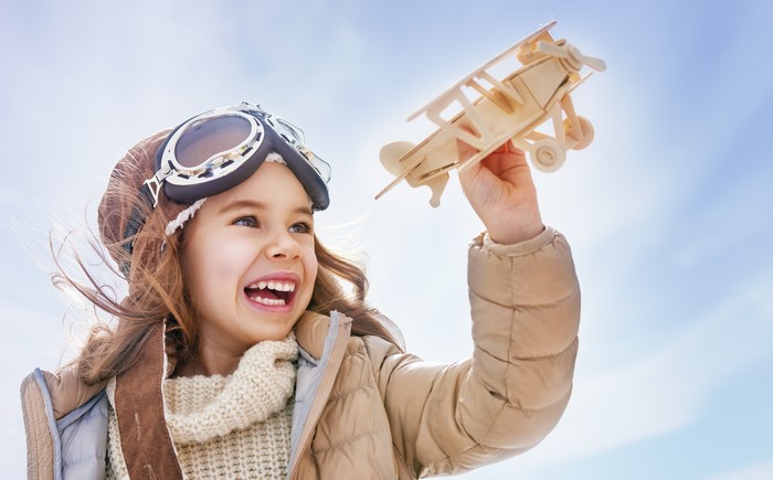 Girl in pilot hat holding toy airplane