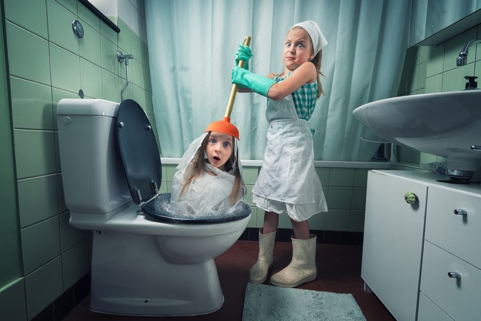 Two girls in a bathroom with a toilet and plunger
