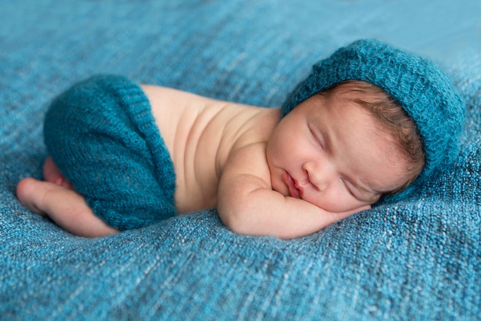 Newborn baby sleeping in a blue hat and pants