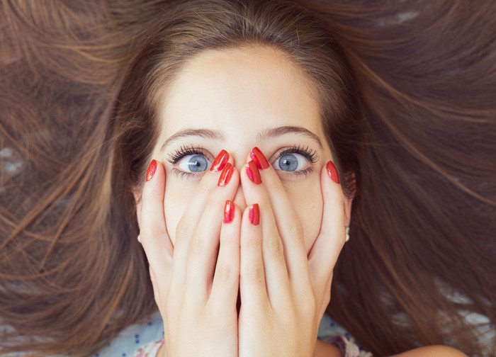 Woman with blue eyes covering her mouth with hands