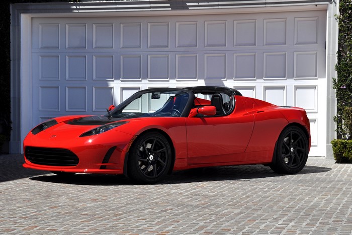 Red Tesla Roadster Sport parked in front of a garage