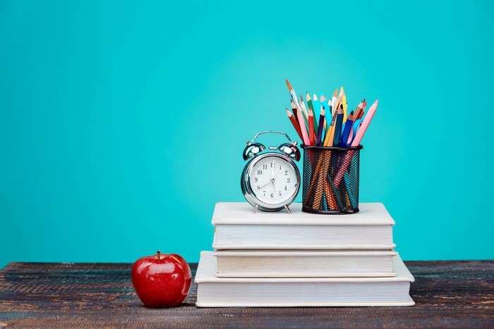 Alarm clock, pencils, books, and apple on a wooden table