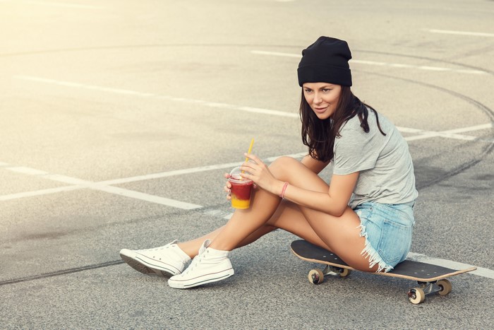 Woman in beanie and denim shorts with skateboard and drink