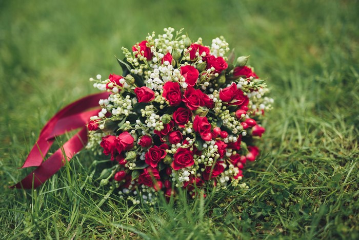 Bouquet of red roses and lilies of the valley on grass
