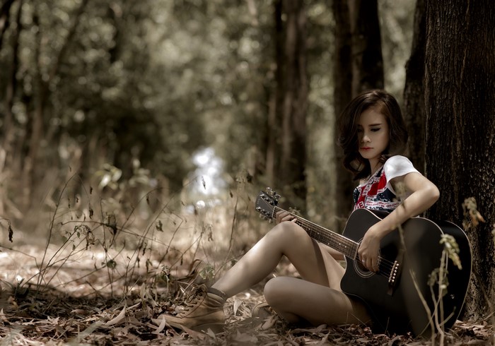 Asian girl playing guitar in forest