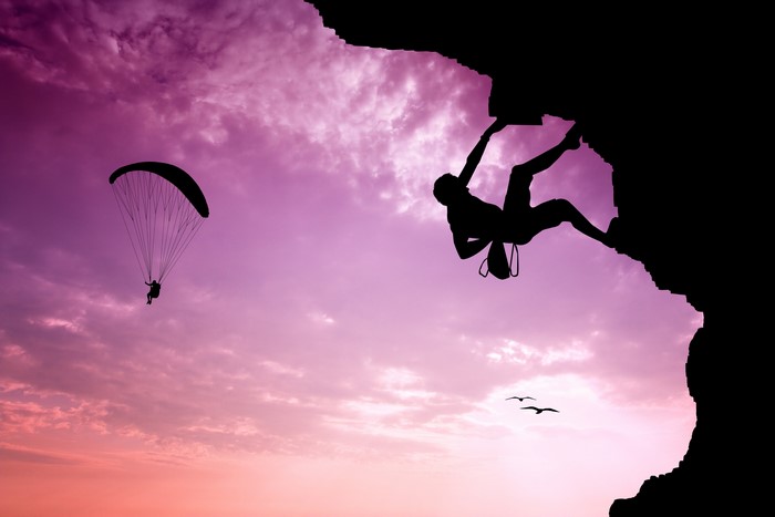 Silhouette of a climber and paraglider against a sunset sky