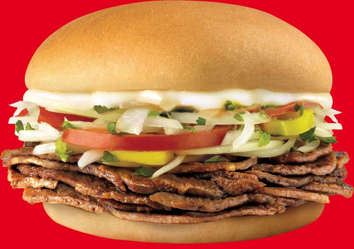 A close-up of a meat sandwich with vegetables and sauce