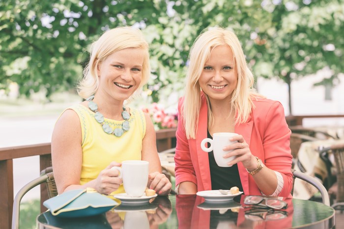 Two blonde girls smiling at a cafe table with cups