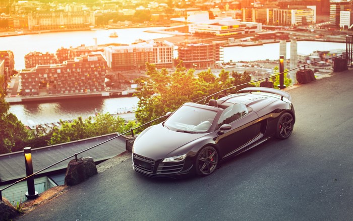 Black Audi R8 GT Spyder convertible on a hill overlooking a city