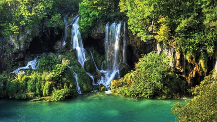 Waterfalls cascading over mossy rocks into a turquoise lake