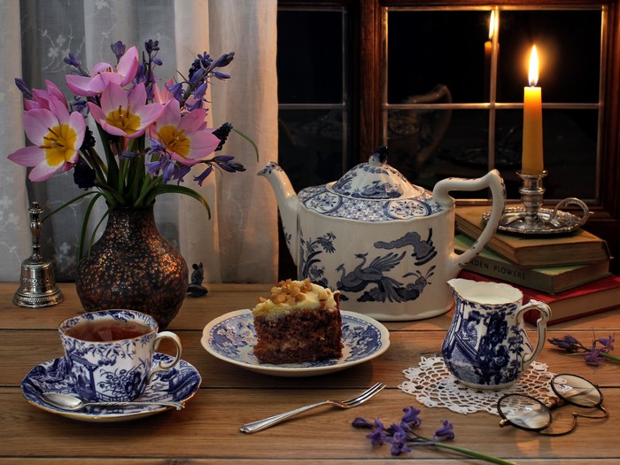 Still life with tea, cake, and flowers by candlelight