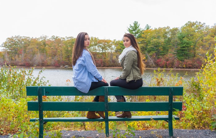 Two girls sitting on a bench by a lake