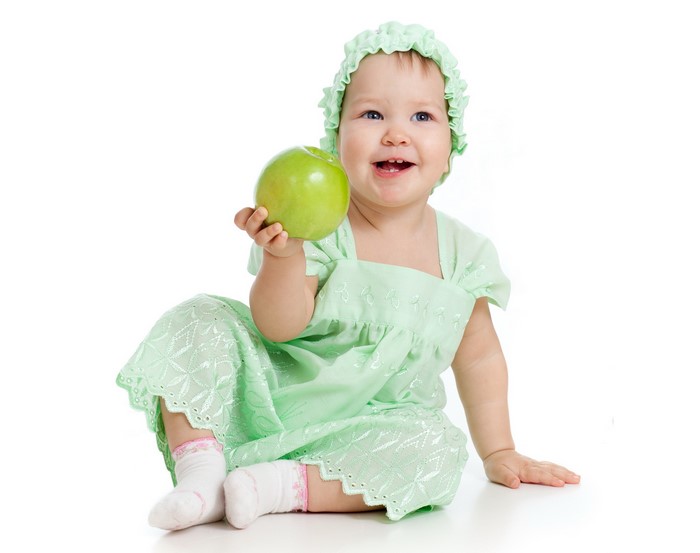 Baby girl in green dress holding an apple