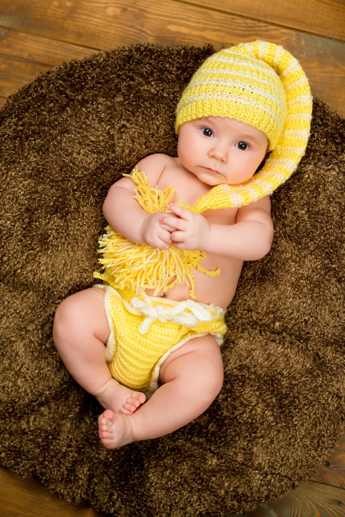 Baby in yellow knitted outfit lying on a brown rug