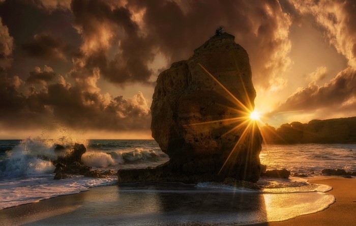 Sunset over the ocean with a large rock formation
