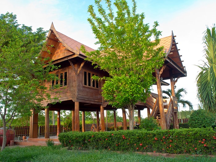 Thai style wooden house on stilts with trees and shrubs