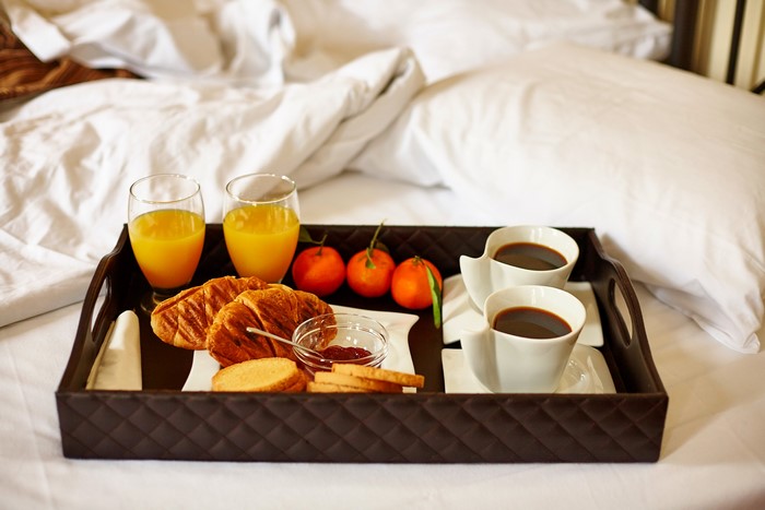 Breakfast tray with coffee, juice, croissants, and fruit on a bed