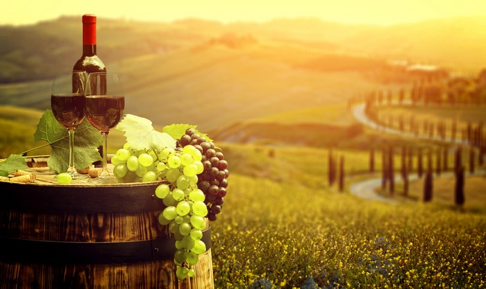 Wine bottle and glasses on barrel with grapes in Tuscany