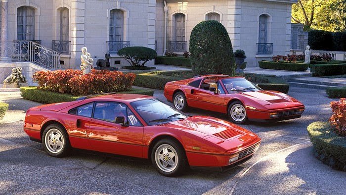 Two red Ferraris parked in front of a mansion