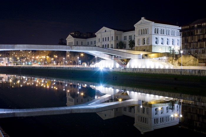 Night view of a bridge and buildings reflected in a canal in Bilbao