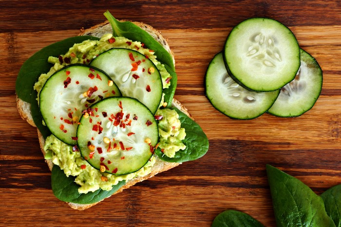 Avocado toast with cucumber and chili flakes on wooden board