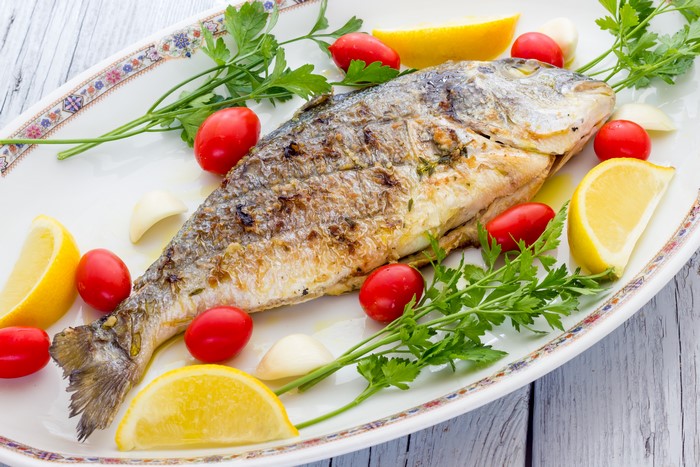 Whole grilled fish with lemon, tomatoes, and parsley on a plate