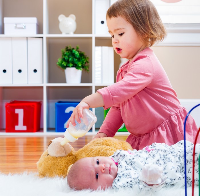 Toddler feeding a baby doll and teddy bear