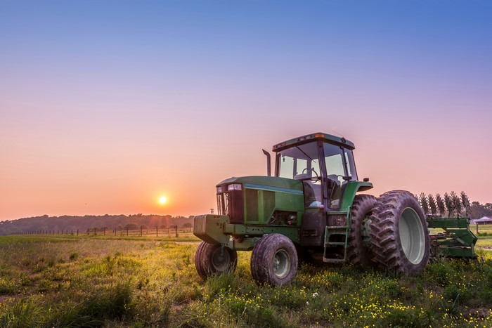 Green tractor in a field at sunset