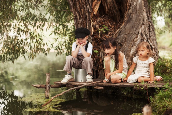 Three children sitting by a tree near water