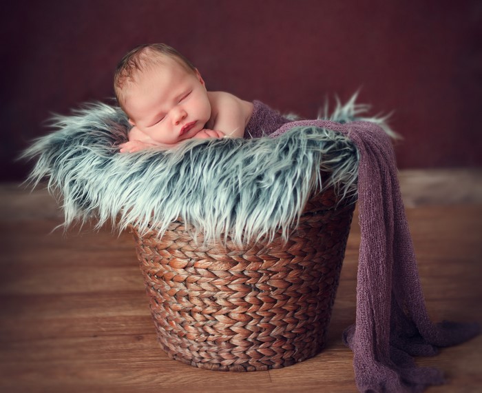 Infant sleeping in a wicker basket with fur and blanket