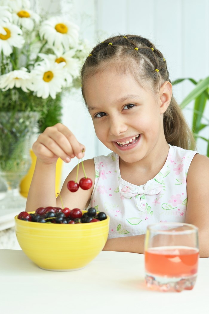 Girl holding cherries with a glass of juice