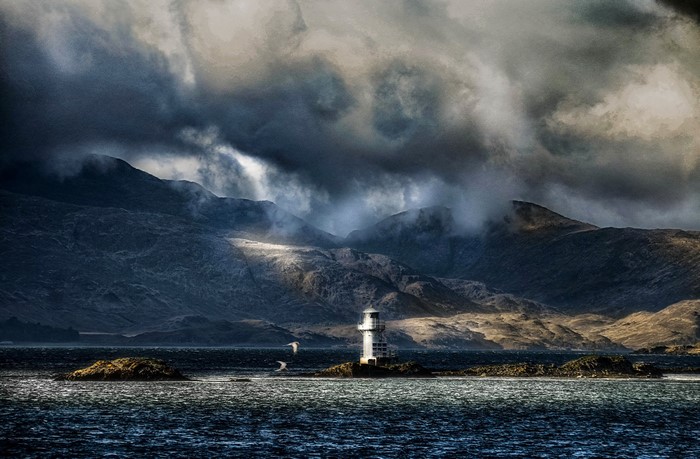 Lighthouse on the coast of Scotland with mountains and clouds