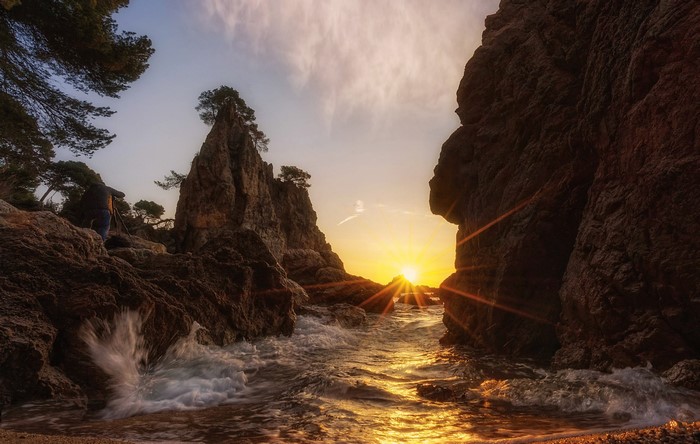 Sunset over rocky coast with waves and sun rays