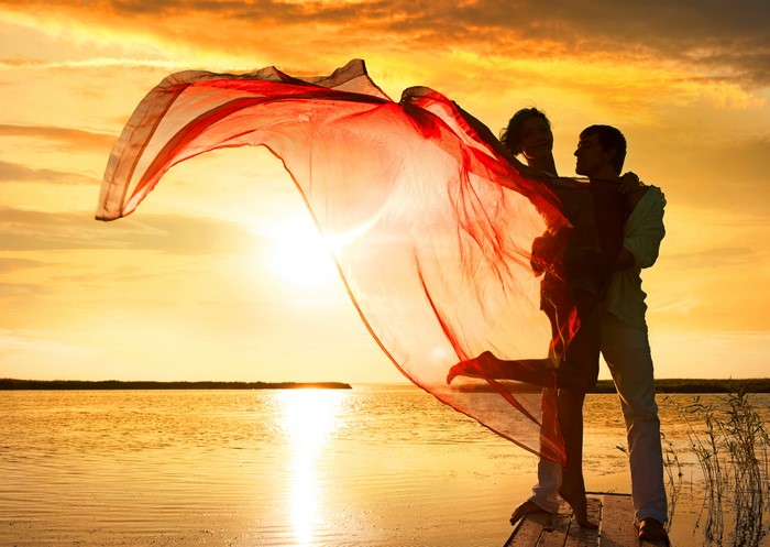 Couple dancing with red fabric at sunset