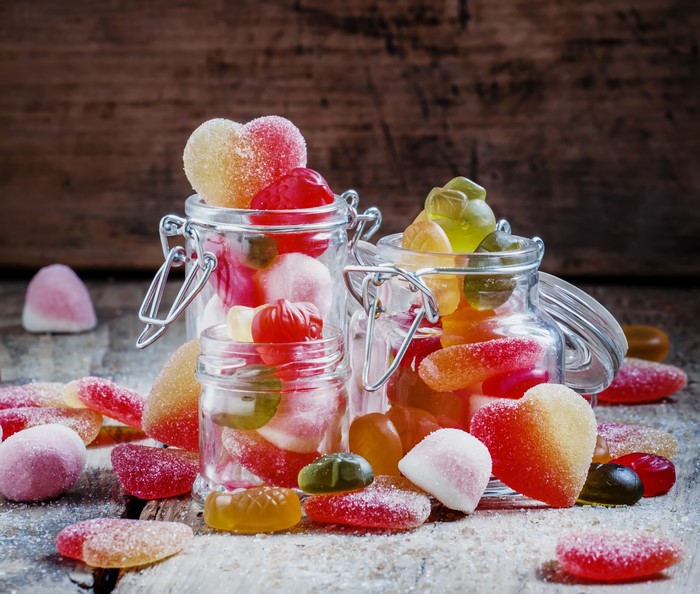 Assorted gummy candies in jars and scattered on a wooden surface
